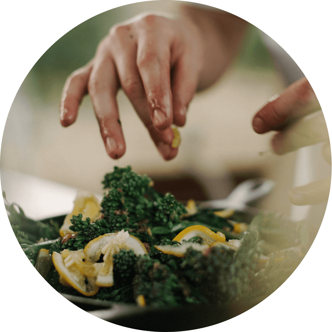 Volunteer's hands mix a salad of broccolini, olive oil and fresh lemon slices